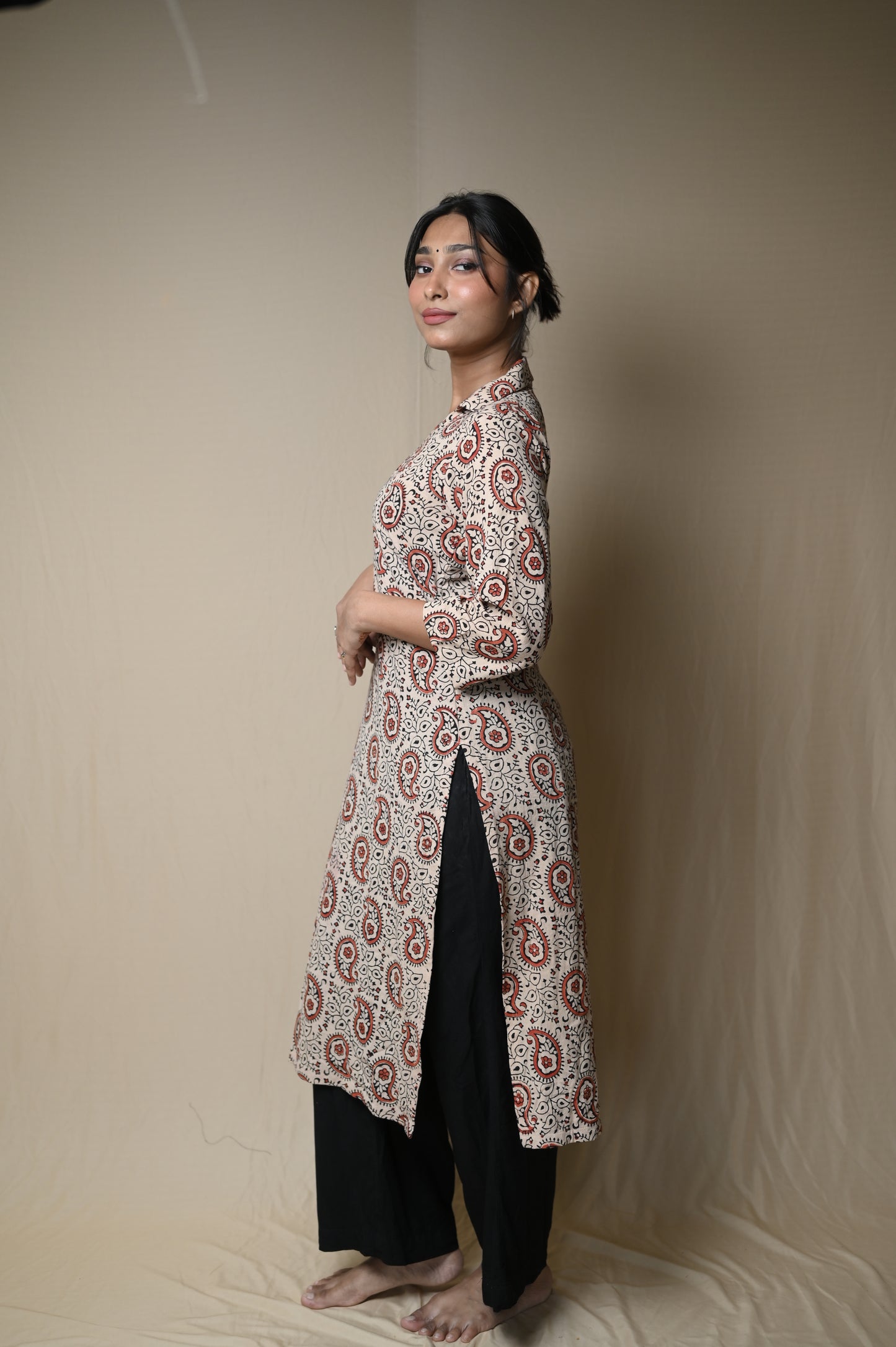 Person lying on a beige surface wearing a patterned top and black pants.