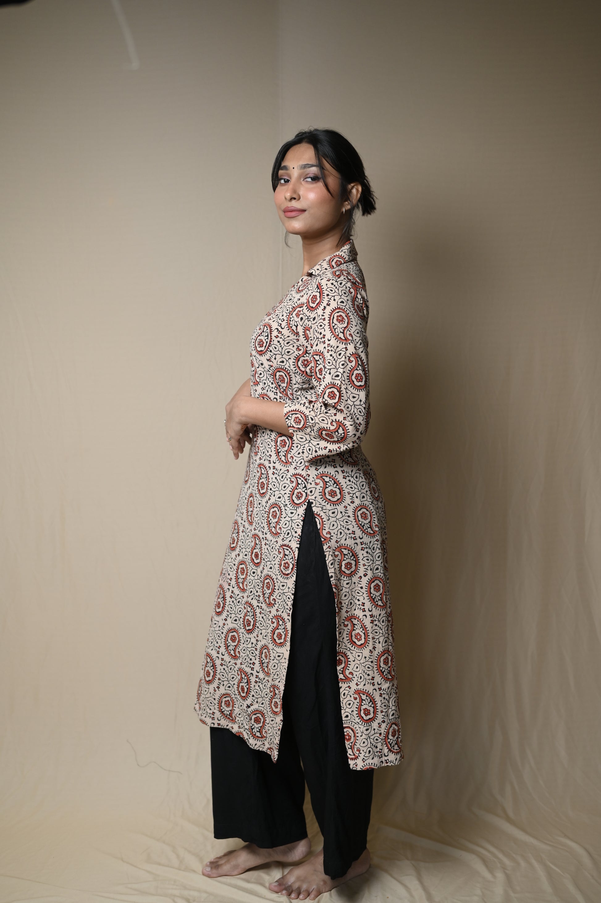 Person lying on a beige surface wearing a patterned top and black pants.